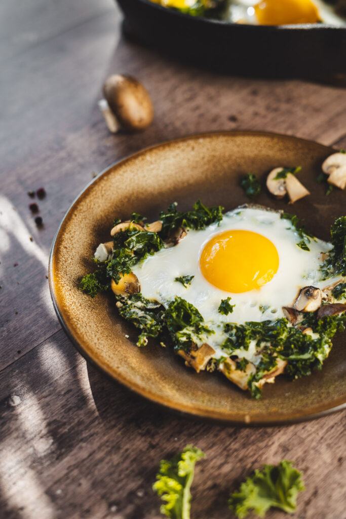 jajka sadzone na jarmużu z dodatkiem pieczarek na talerzu